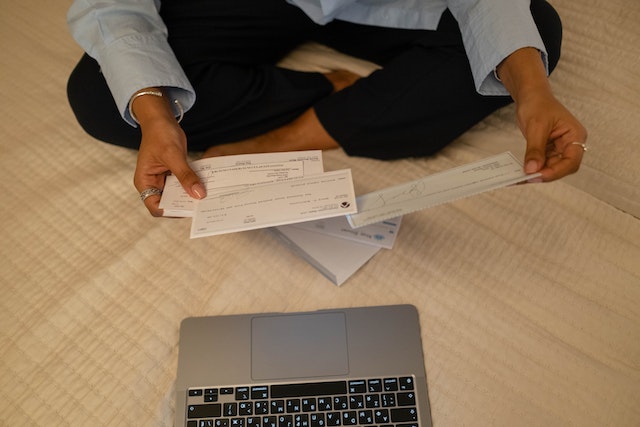 someone looking at cheques in front of a laptop on a bed